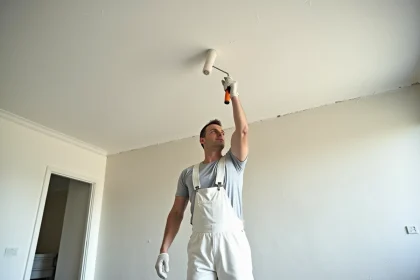 Peintre professionnel appliquant de la peinture blanche sur un plafond abîmé de 50m2 dans un appartement