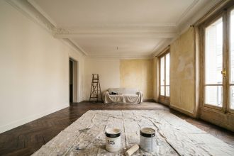 Salon d'appartement haussmannien avec moulures au plafond, moitié des murs repeints en blanc cassé mat contrastant avec l'ancienne peinture jaunie et le parquet en chevrons